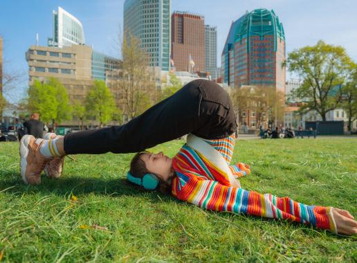 Meisje in gekleurde trui in yoga-houding met Den Haag als achtergrond