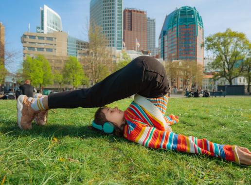 Meisje in gekleurde trui in yoga-houding met Den Haag als achtergrond