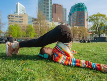 Meisje in gekleurde trui in yoga-houding met Den Haag als achtergrond