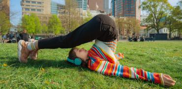 Meisje in gekleurde trui in yoga-houding met Den Haag als achtergrond